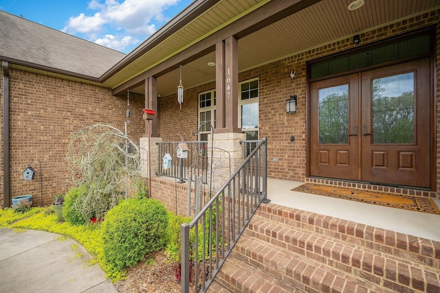 view of exterior entry with roof with shingles, french doors, covered porch, and brick siding
