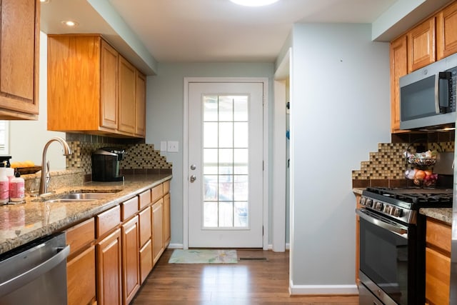 kitchen with wood finished floors, a sink, light stone countertops, and stainless steel appliances