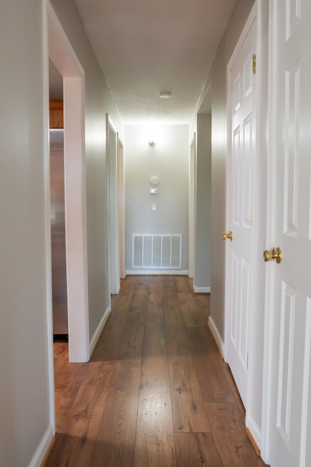 hall with baseboards, visible vents, and hardwood / wood-style flooring