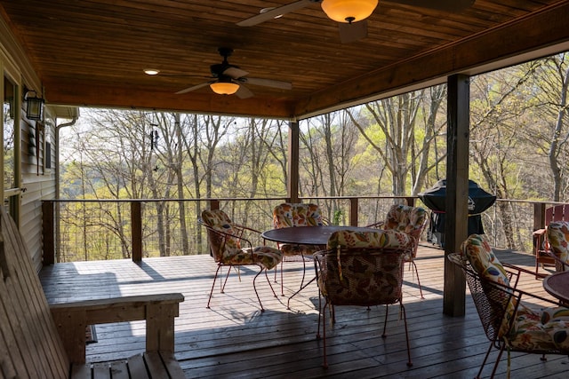 sunroom featuring a wooded view, a ceiling fan, and plenty of natural light
