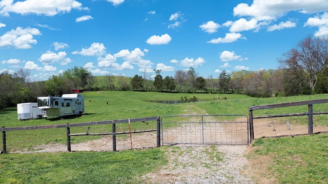 view of gate featuring a rural view, fence, and a lawn