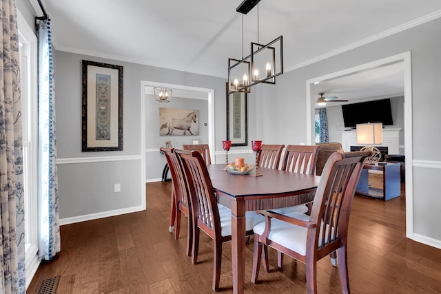 dining room with crown molding, ceiling fan with notable chandelier, wood finished floors, and a fireplace