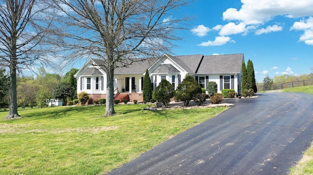 ranch-style house with aphalt driveway, a front yard, fence, brick siding, and a shingled roof