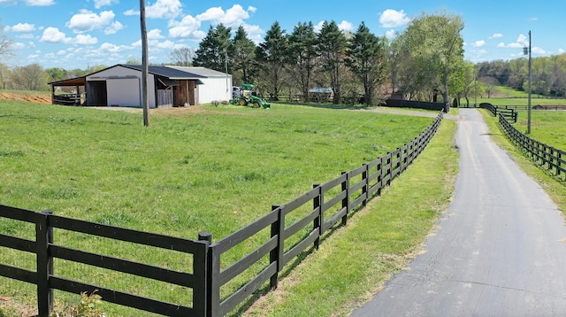 view of yard with an outdoor structure, driveway, a rural view, an outbuilding, and fence