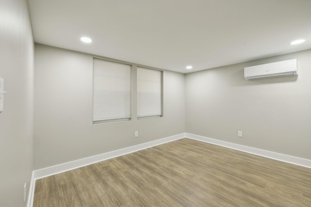 below grade area featuring a wall mounted air conditioner, recessed lighting, baseboards, and wood finished floors