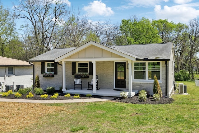 view of front of home with board and batten siding, cooling unit, covered porch, a front yard, and brick siding