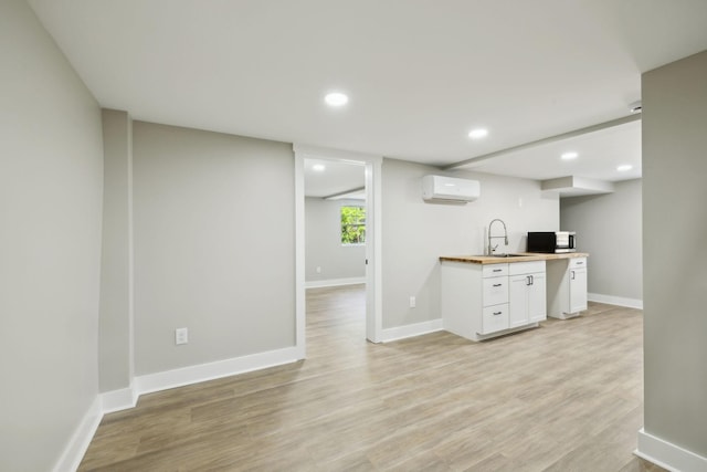 kitchen with butcher block counters, white cabinetry, a wall mounted AC, stainless steel microwave, and a sink