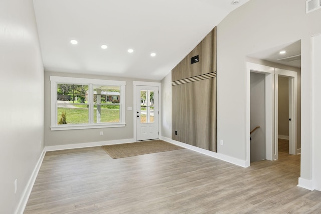 foyer with visible vents, baseboards, light wood-style floors, and vaulted ceiling