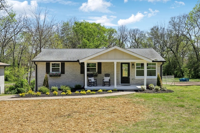 single story home featuring a shingled roof, covered porch, a front yard, and brick siding