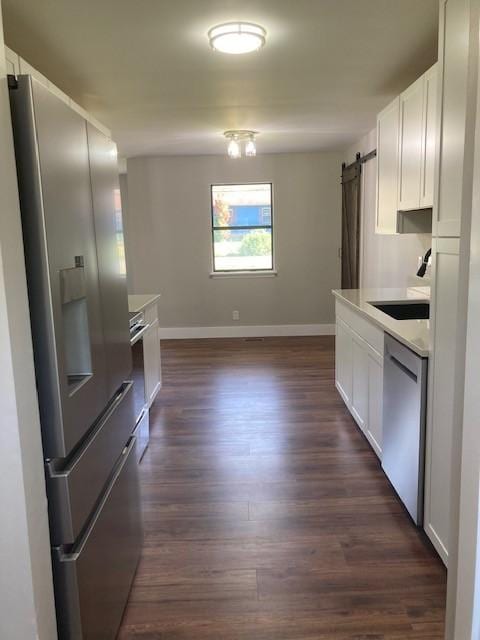 kitchen with baseboards, dark wood-type flooring, a barn door, stainless steel appliances, and a sink