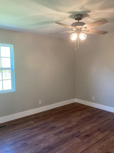 empty room with dark wood-style flooring, visible vents, baseboards, and a ceiling fan