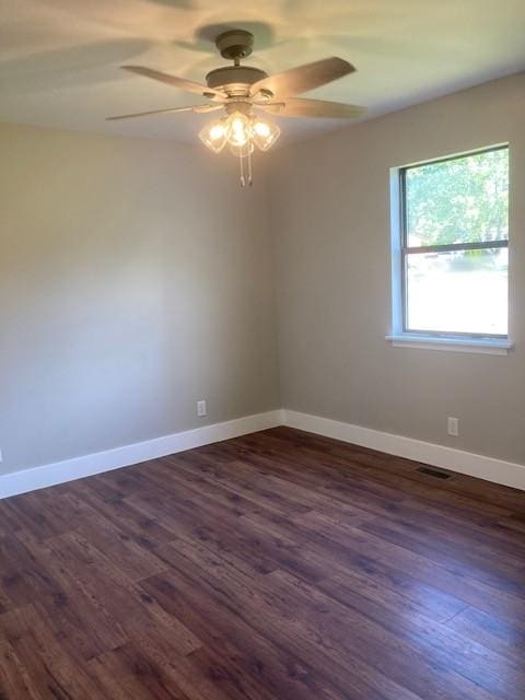 empty room with dark wood-type flooring, visible vents, baseboards, and ceiling fan