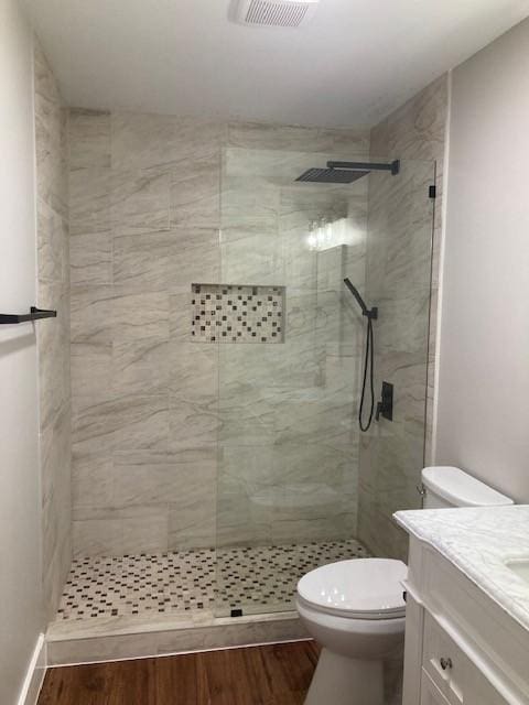 bathroom featuring vanity, toilet, a walk in shower, visible vents, and wood finished floors