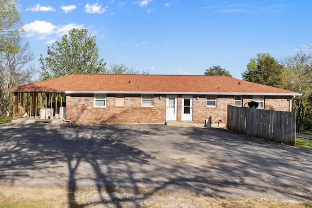 rear view of property with a shingled roof, aphalt driveway, and brick siding