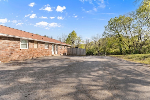 view of property exterior with brick siding, entry steps, fence, and aphalt driveway