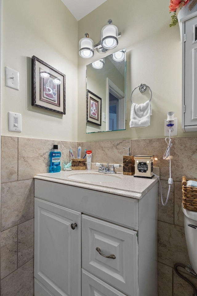 half bath featuring toilet, tile walls, vanity, and wainscoting
