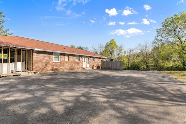 rear view of property featuring brick siding, driveway, and fence