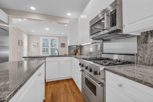 kitchen featuring white cabinetry, a sink, stainless steel appliances, light wood finished floors, and backsplash