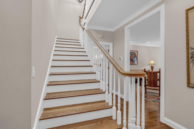 stairway with wood finished floors, baseboards, and ornamental molding