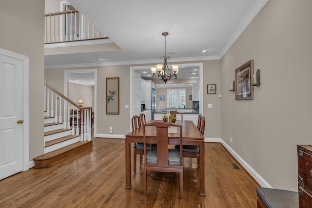 dining room featuring a chandelier, wood finished floors, visible vents, and stairs