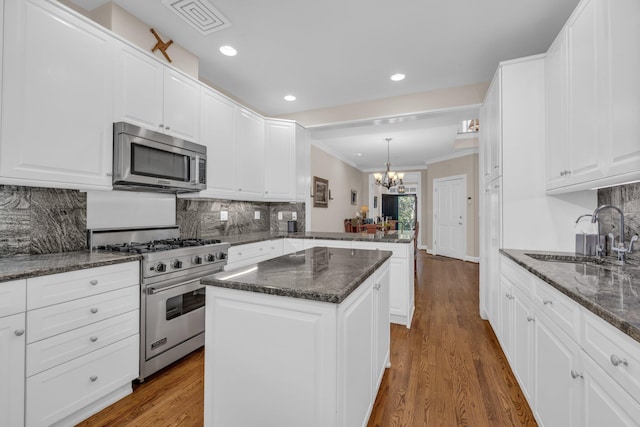 kitchen featuring an inviting chandelier, a sink, ornamental molding, a peninsula, and stainless steel appliances