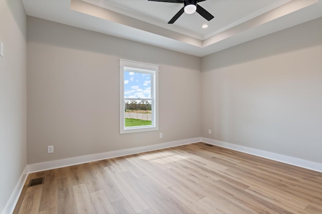 spare room featuring visible vents, baseboards, light wood-type flooring, a ceiling fan, and a tray ceiling