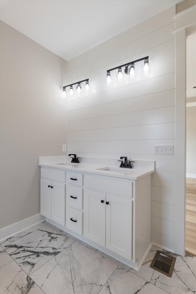 bathroom with double vanity, marble finish floor, a sink, and baseboards