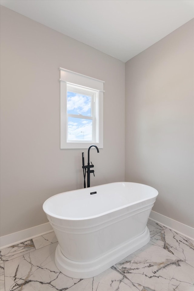 full bath with a freestanding bath, marble finish floor, and baseboards