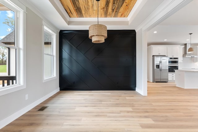 interior space with baseboards, wall chimney range hood, visible vents, a raised ceiling, and appliances with stainless steel finishes