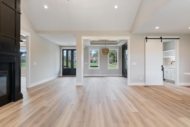 unfurnished living room with light wood-style flooring, a fireplace, baseboards, and a barn door