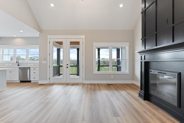 unfurnished living room with a healthy amount of sunlight, light wood-style floors, french doors, and lofted ceiling