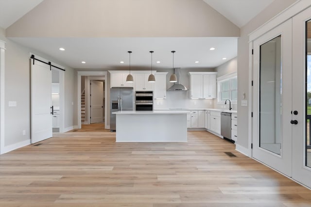 kitchen featuring vaulted ceiling, wall chimney range hood, a center island, a barn door, and stainless steel appliances