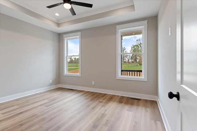 spare room featuring visible vents, baseboards, a raised ceiling, light wood-type flooring, and a ceiling fan
