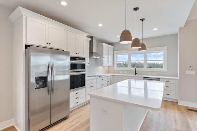 kitchen with light wood-type flooring, wall chimney range hood, white cabinets, a kitchen island, and stainless steel appliances