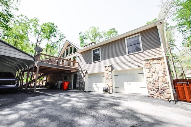 back of property featuring a garage, stone siding, stairs, driveway, and a deck