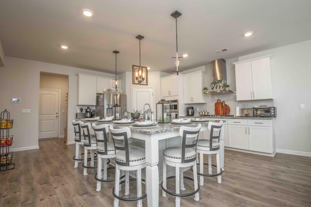 kitchen with a kitchen island with sink, wall chimney range hood, dark wood-style floors, and stainless steel appliances