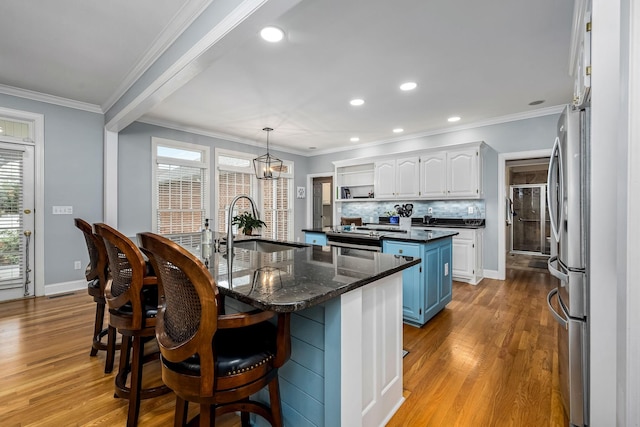 kitchen with white cabinets, a center island with sink, stainless steel appliances, light wood finished floors, and a sink