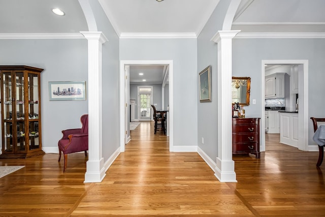 hallway with light wood-type flooring, decorative columns, baseboards, and ornamental molding
