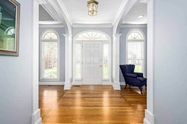 foyer entrance featuring arched walkways, light wood finished floors, baseboards, and crown molding