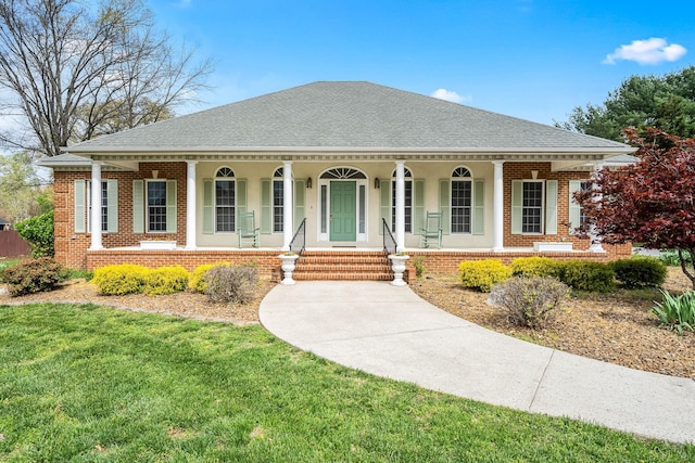 view of front of property featuring a shingled roof, a front yard, covered porch, and brick siding