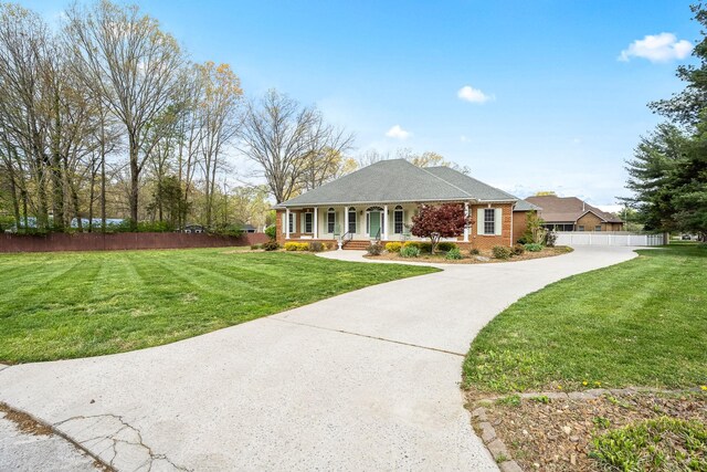 single story home featuring a porch, a front yard, fence, brick siding, and driveway