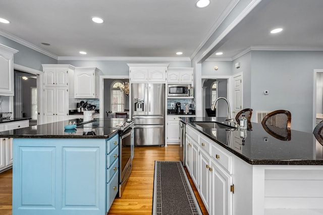 kitchen with white cabinets, a sink, appliances with stainless steel finishes, a center island with sink, and blue cabinets