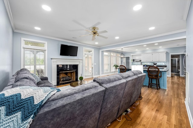 living room featuring a wealth of natural light, light wood-style floors, a ceiling fan, and crown molding