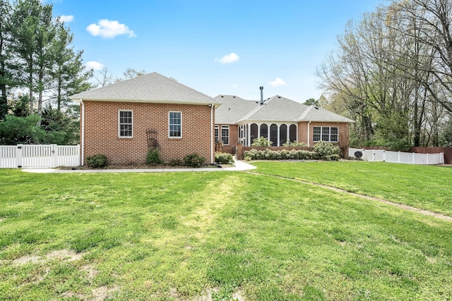 rear view of property with fence, brick siding, a gate, and a lawn