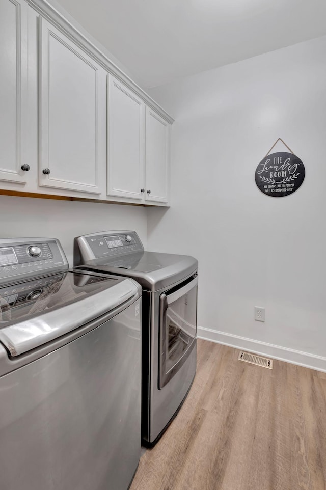 washroom with light wood-style flooring, visible vents, washing machine and clothes dryer, and cabinet space