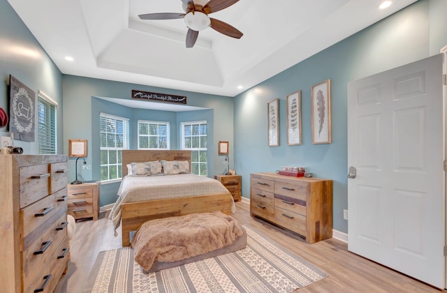 bedroom with a tray ceiling, light wood finished floors, baseboards, and recessed lighting