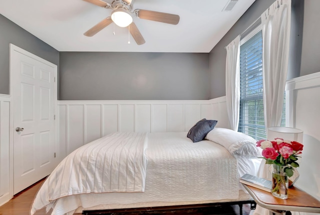 bedroom with visible vents, ceiling fan, wainscoting, and wood finished floors