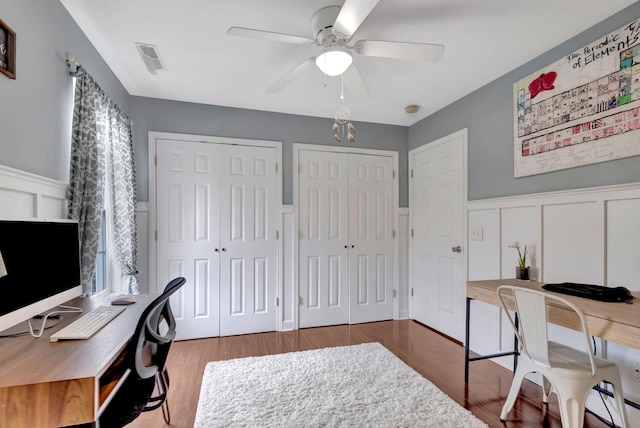 office featuring a decorative wall, ceiling fan, wood finished floors, and a wainscoted wall