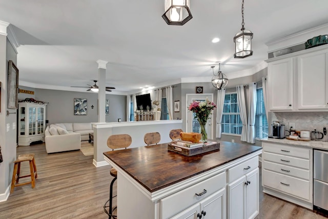 kitchen featuring a ceiling fan, ornamental molding, white cabinets, a breakfast bar, and open floor plan