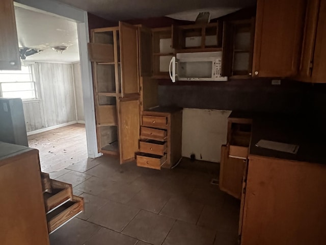 kitchen featuring dark tile patterned floors, white microwave, glass insert cabinets, and open shelves